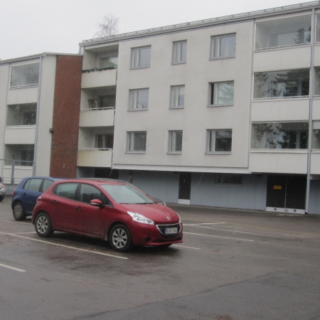 Talo 1, parvekkeet ja ikkunat länteen. Etualalla ulkona olevat autopaikat.